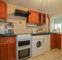A kitchen with wooden cabinets a stove microwave toaster washing machine and dishwasher at Derwent Edge in Portinscale