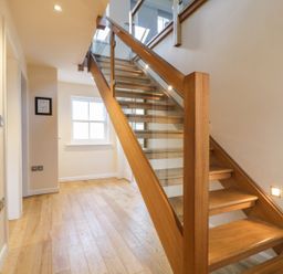A wooden staircase with glass panels along one side in a hallway with wooden flooring and a window at Wrenville in Keswick