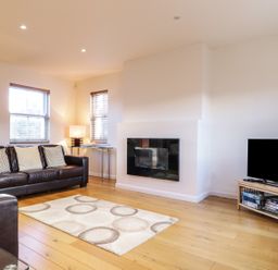 A living room with a brown leather sofa a rug a wall-mounted fireplace and a TV on a wooden stand at Wrenville in Keswick