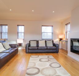 A living room with two brown leather sofas a patterned rug wooden floor and windows at Wrenville in Keswick