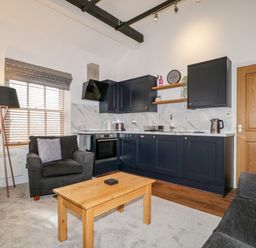 A living room with a wooden coffee table two armchairs carpet and a kitchen with black cabinets and marble backsplash at The Old Hayloft in Keswick