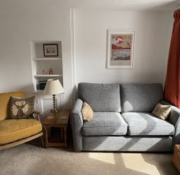 A living room with a sofa, armchair, lamp, and bookshelf at Prospect Lodge in Portinscale