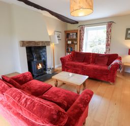 A living room with two red sofas a wood burning stove and a wooden coffee table at Mell View Cottage in Ullswater