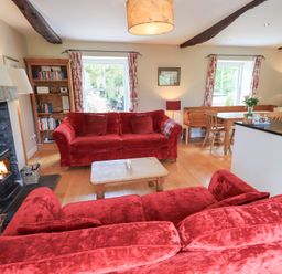 A living room with red sofas wooden coffee table bookshelf and wood burning stove at Mell View Cottage in Ullswater