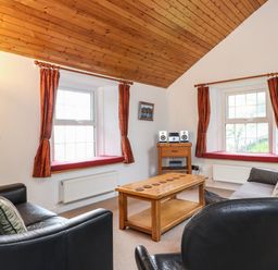 A living room with wooden ceiling brown curtains and black leather sofas at Coombe Cottage in Borrowdale