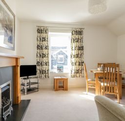 A living room with a fireplace television dining table with chairs and patterned curtains at Helvellyn in Keswick