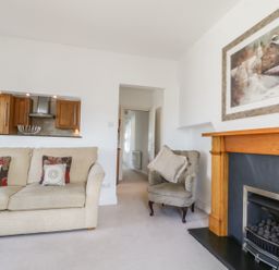 A living room with a beige sofa with cushions a grey armchair a wooden fireplace and a painting above the fireplace at Helvellyn in Keswick