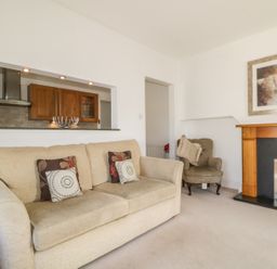 A living room with a beige sofa and armchair a fireplace and a view into the kitchen at Helvellyn Keswick