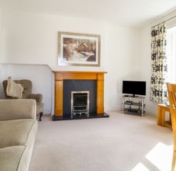 A living room with a fireplace armchairs a television and wooden dining chairs at Helvellyn in Keswick