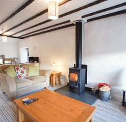 A living room with a beige sofa green and patterned cushions a wood burning stove wooden coffee table dining table and chairs at Laurel Cottage in Spark Bridge