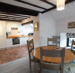 A kitchen and dining area with wooden table and chairs and white cabinets at Laurel Cottage in Spark Bridge