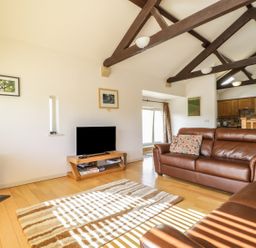 A living room with brown leather sofas a wooden TV stand with a television a patterned rug and exposed wooden beams at Skiddaw in Cockermouth