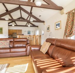 A living room with brown leather sofas wooden beams on the ceiling and a kitchen area at Skiddaw in Cockermouth