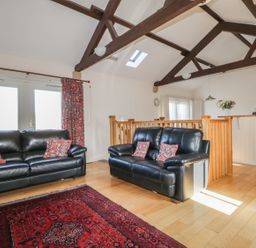 A living room with two black leather sofas and patterned cushions next to a red rug at Esthers Barn in Cockermouth