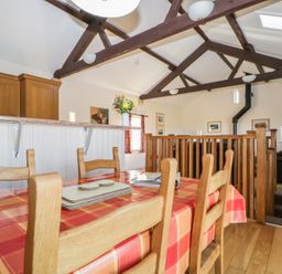 A dining area with a wooden table and chairs next to a kitchen counter in a room with exposed wooden beams and a railing at Esthers Barn in Cockermouth