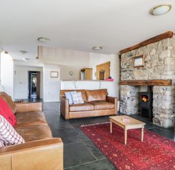 A living room with two brown leather sofas a red rug a wooden coffee table a stone fireplace with a wood stove and a television on a stand at Beckside in Cockermouth