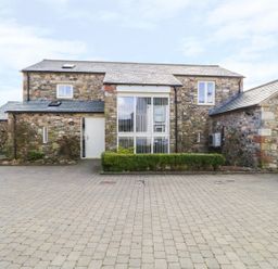 A stone house with a paved driveway and green bushes at Beckside in Cockermouth