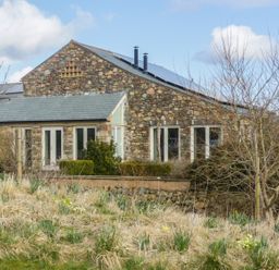 A stone house with multiple windows and solar panels on the roof surrounded by dry grass and leafless trees at Beckside in Cockermouth