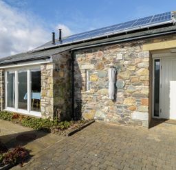 The exterior of a stone house with solar panels on the roof a white door and sliding glass doors at Buttermere in Cockermouth