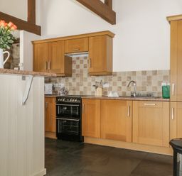 A kitchen with wooden cabinets a stove a sink a trash bin and flowers on a counter at Buttermere in Cockermouth