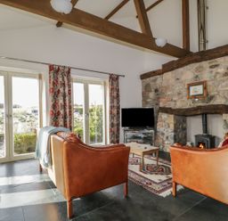 A living room with leather sofas a stone fireplace a flat screen tv and large windows with floral curtains at Buttermere in Cockermouth
