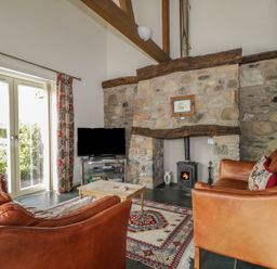 A living room with two leather sofas a wooden coffee table a television a stone fireplace and a patterned rug at Buttermere in Cockermouth