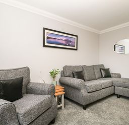 A living room with two grey sofas, a small wooden side table with a plant, a landscape picture on the wall, and an oval mirror at Andra Ghyll in Keswick