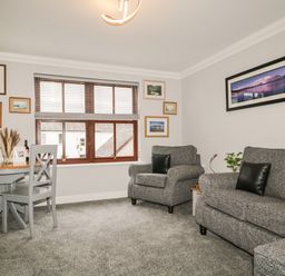 A living room with grey sofa and armchair a wooden table and chairs and framed pictures on the walls at Andra Ghyll in Keswick