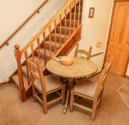 A small dining area with a round wooden table and three chairs next to a carpeted staircase at Juniper Cottage in Ambleside