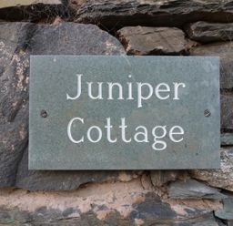 A stone plaque with the text Juniper Cottage mounted on a stone wall at Juniper Cottage Ambleside