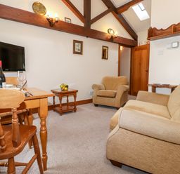 A sitting room with a sofa armchair wooden dining table and television at The Hayloft in Thirlmere