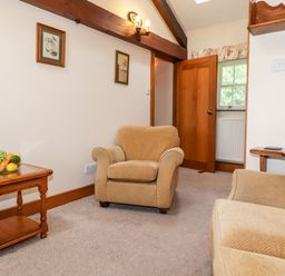 A sitting area with beige armchairs wooden side tables and framed pictures on the wall at The Hayloft in Thirlmere