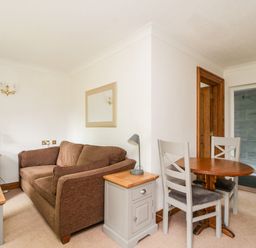 A small living room with a brown sofa a wooden table with two chairs a side table with a lamp and a mirror on the wall at Thirlmere Suite in Thirlmere