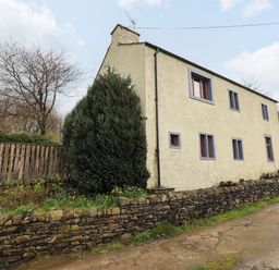 A stone wall and a house with multiple windows beside a dirt road at Scales Cottage in Lorton near Cockermouth