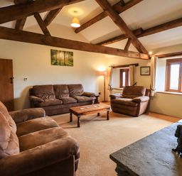 A living room with brown sofas wooden beams on ceiling a wooden coffee table and a statue of a dog on the fireplace at Scales Cottage in Lorton near Cockermouth