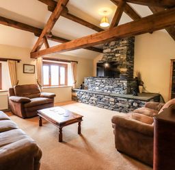 A living room with wooden beams stone fireplace brown sofas and a wooden coffee table at Scales Cottage in Lorton near Cockermouth