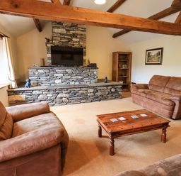 A living room with brown sofas a wooden coffee table and a stone fireplace at Scales Cottage in Lorton near Cockermouth