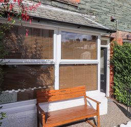A wooden bench outside a window with closed blinds next to a black door at Archers in Keswick
