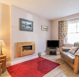 A living room with a sofa a television a wall-mounted fireplace a red rug and a lamp at Swinside Cottage in Keswick