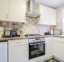 A kitchen with cream cabinets a tiled backsplash and countertop with appliances and a window at Swinside Cottage in Keswick