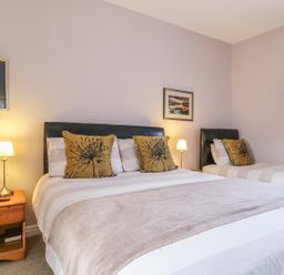 A bedroom with a double bed and a single bed two bedside tables with lamps and wall art at Swinside Cottage in Keswick