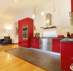 A kitchen with red cabinets stainless steel appliances and an armchair with a lamp in the corner at Keswick Loft in Keswick