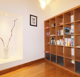 A wooden bookshelf with books and board games next to a white wall with a recessed shelf holding a white vase with two branches at Keswick Loft in Keswick