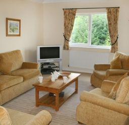 A living room with upholstered armchairs and a sofa around a wooden coffee table with tea set and a television at Whitbarrow Holiday Village Troutbeck 5 Ullswater
