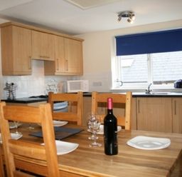 A kitchen with wooden dining table set with plates and wine bottle at Whitbarrow Holiday Village Troutbeck 5 in Ullswater