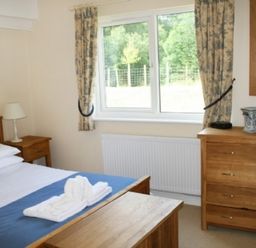 A bedroom with a bed side table lamp dresser and a window with curtains at Whitbarrow Holiday Village Troutbeck 5 Ullswater