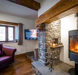 A living room with a stone fireplace a wood burning stove a purple sofa and a TV mounted on the wall at Grayrigg Foot Stable in Grayrigg