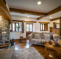 A living room with a plaid sofa wooden coffee table stone fireplace and dining area at Grayrigg Foot Stable in Grayrigg