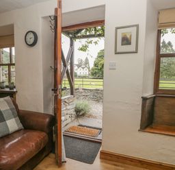 An open door leading outside with a brown leather sofa and a window with wooden bench seating at Tanner Croft Cottage in Grasmere