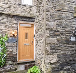 Stone exterior wall with a wooden door and a window with flower baskets at Granary Nook in Windermere